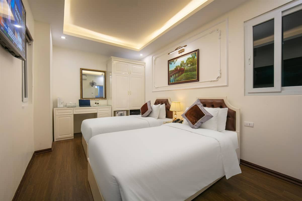 A hotel room with two beds, a desk, a TV, and a painting on the wall.