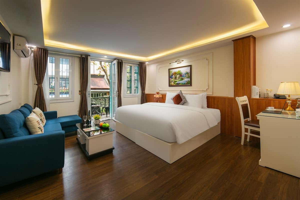A hotel room with a bed, a sofa, a desk, and a window with curtains.