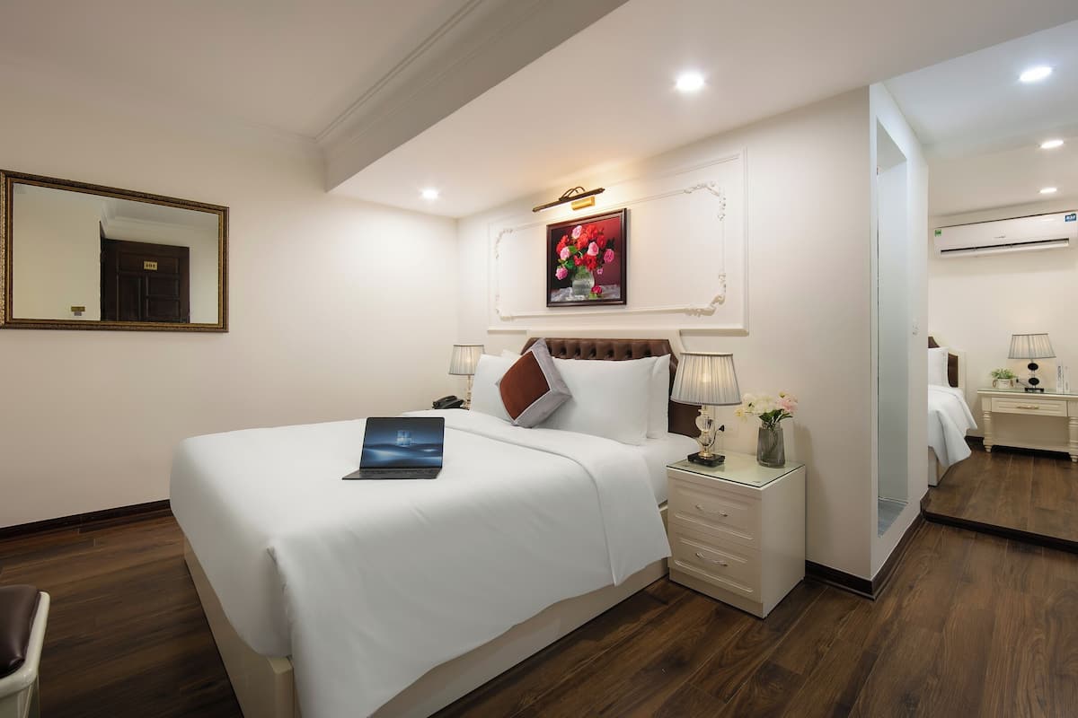 A hotel room with a large bed, bedside tables, a mirror, and a painting on the wall.