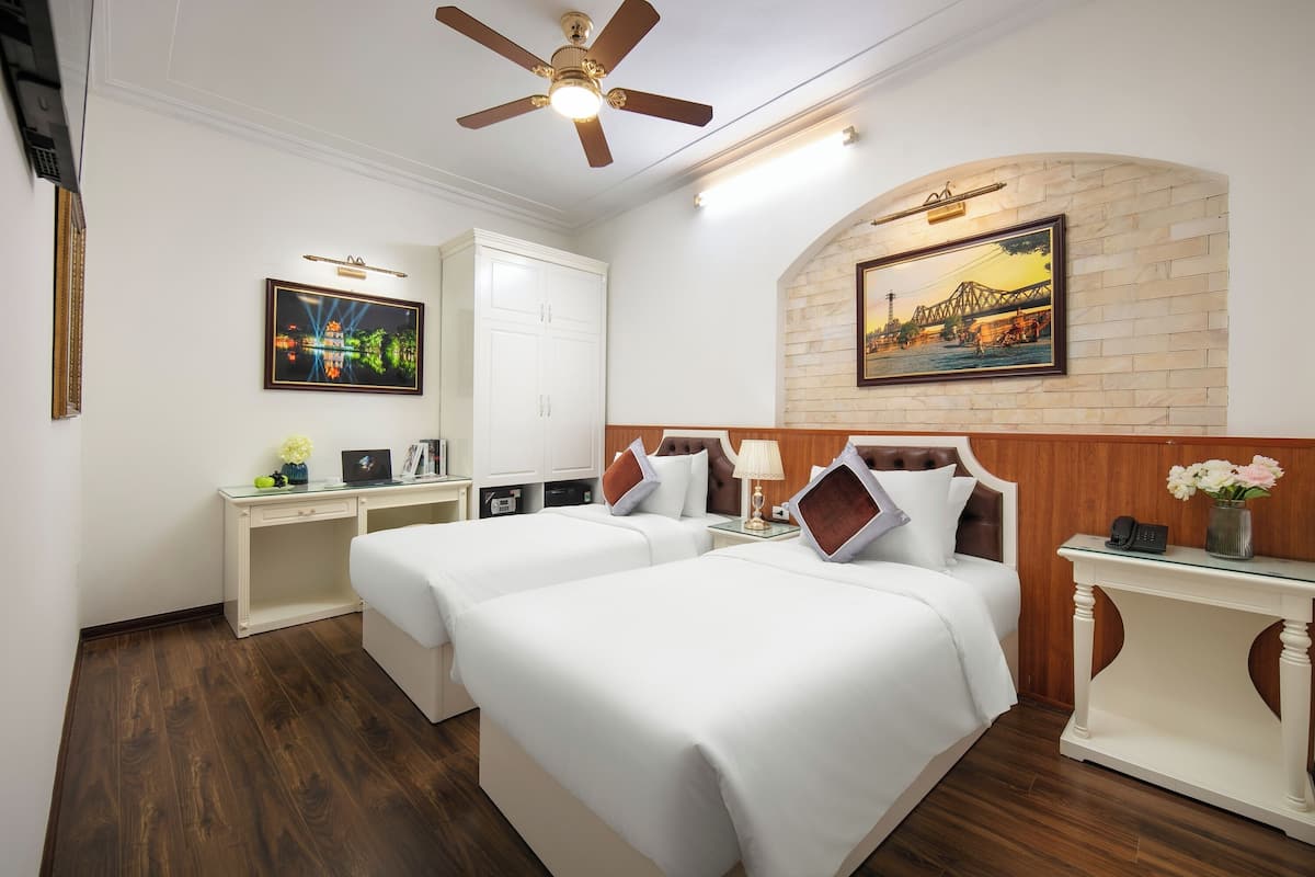 A hotel room with two beds, a desk, a wardrobe, a ceiling fan, and a mural on the wall.