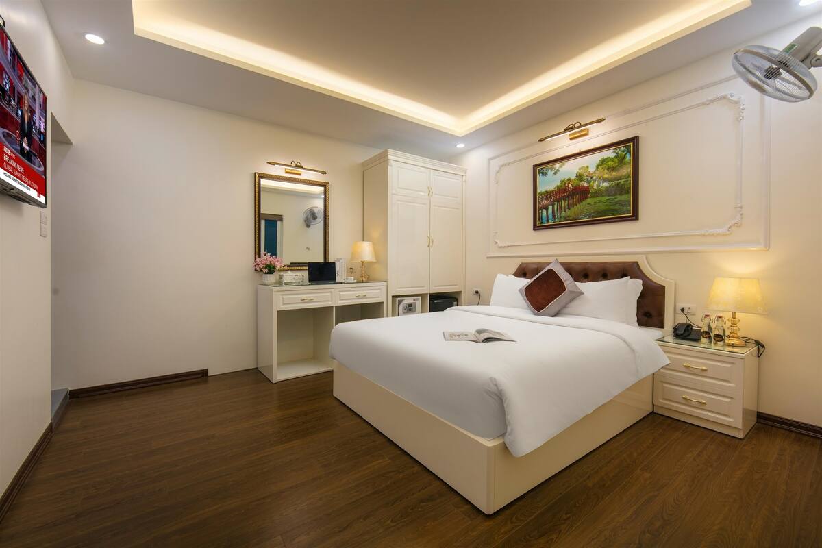 A hotel room with a large bed, a desk, a wardrobe, and a ceiling fan.