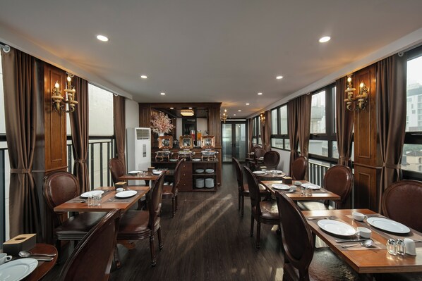 Un comedor con mesas y sillas de madera, una isla central con estaciones de buffet y ventanas grandes con cortinas.