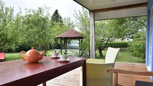 Una terraza de madera con una mesa y sillas, un pabellón al fondo y vista a un jardín.
