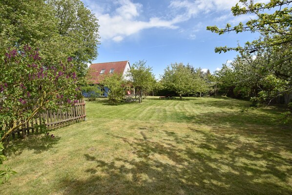 Een verzorgd gazon met houten omheining, bomen en een huis met een rood dak.