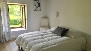 Une chambre à coucher avec un lit, une fenêtre, une lampe fixée au mur et un tableau encadré.
