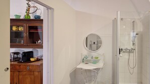A bathroom with a shower, a small sink with a mirror, and a wooden cabinet with kitchen appliances.