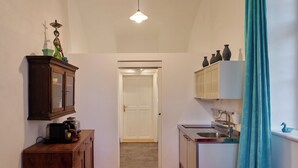 A narrow hallway with wooden flooring, a kitchen area with a sink and cabinets, and a door leading to another room.
