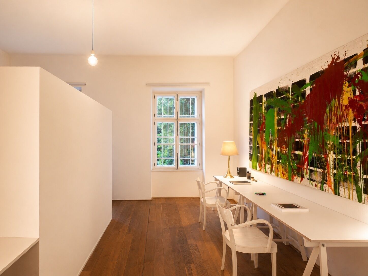 A modern room with a white desk, chairs, a lamp, and a large abstract painting on the wall.
