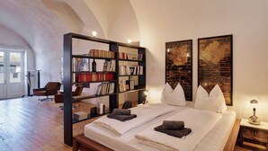 Un dormitorio espacioso con una cama grande, una estantería y dos cuadros grandes en la pared.