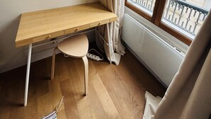 Een hoekappartement met een houten bureau, een stoel, een raam met gordijnen en uitzicht op gebouwen.