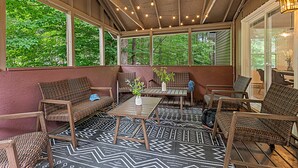 A covered outdoor seating area with wicker furniture, a patterned floor, and string lights.