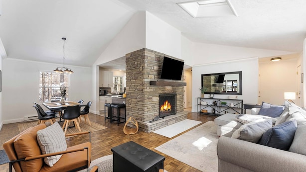 A modern living room with a stone fireplace, a dining area with a large window, and a cozy seating arrangement.