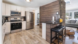 A modern kitchen with stainless steel appliances, a wooden accent wall, and a bar area with stools.