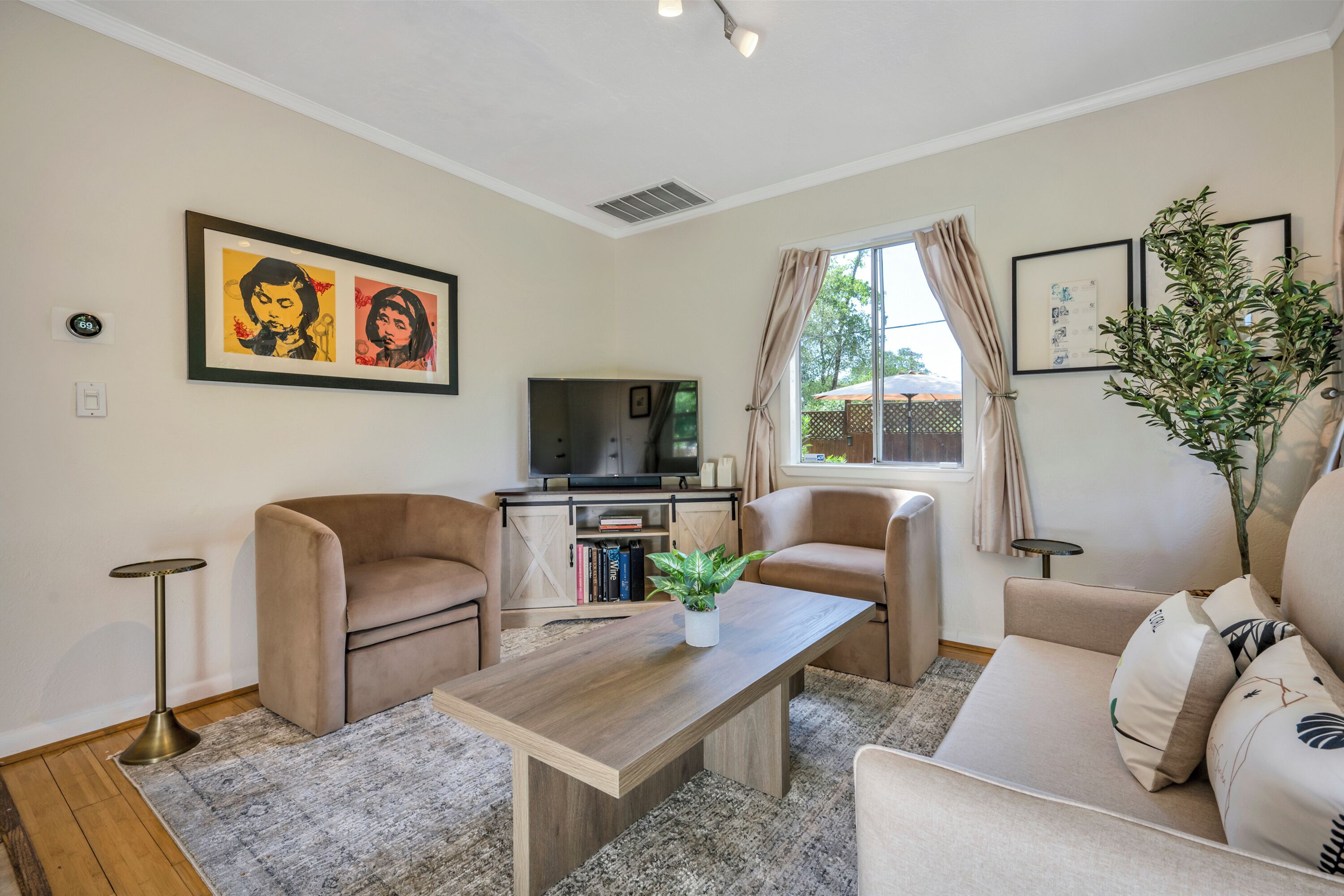 Een woonkamer met een houten salontafel, beige banken, een televisie en lijstwerken aan de muur.
