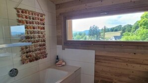 Une salle de bain au décor intérieur en bois, dotée d’une grande fenêtre et d’un présentoir à fruits fixé au mur.