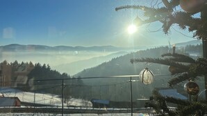 Un paysage enneigé sous un ciel dégagé, un sapin de Noël décoré et un soleil qui brille à travers une fenêtre.