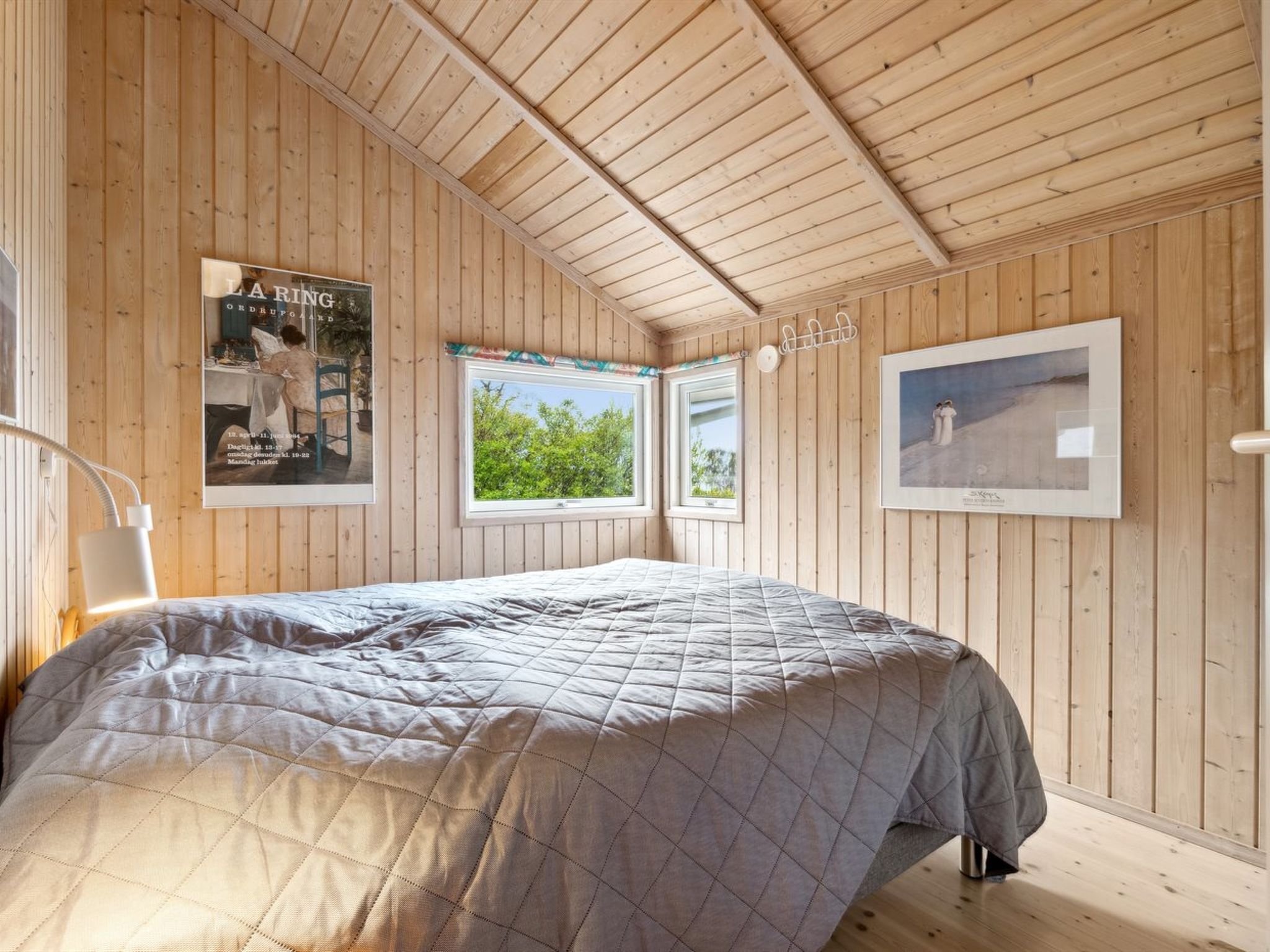 Een kamer met houten lambrisering, een bed, twee ramen en afbeeldingen in lijsten aan de wanden.