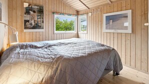 Ein Zimmer mit Holzwänden, einem Bett, zwei Fenstern und gerahmten Bildern an den Wänden.