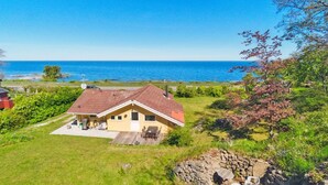 Ein Haus mit rotem Dach, einer kleinen Veranda und Blick aufs Meer.