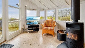 Ein gemütliches Zimmer mit großem Fenster, Fernseher, Korbsessel und Kaminofen.