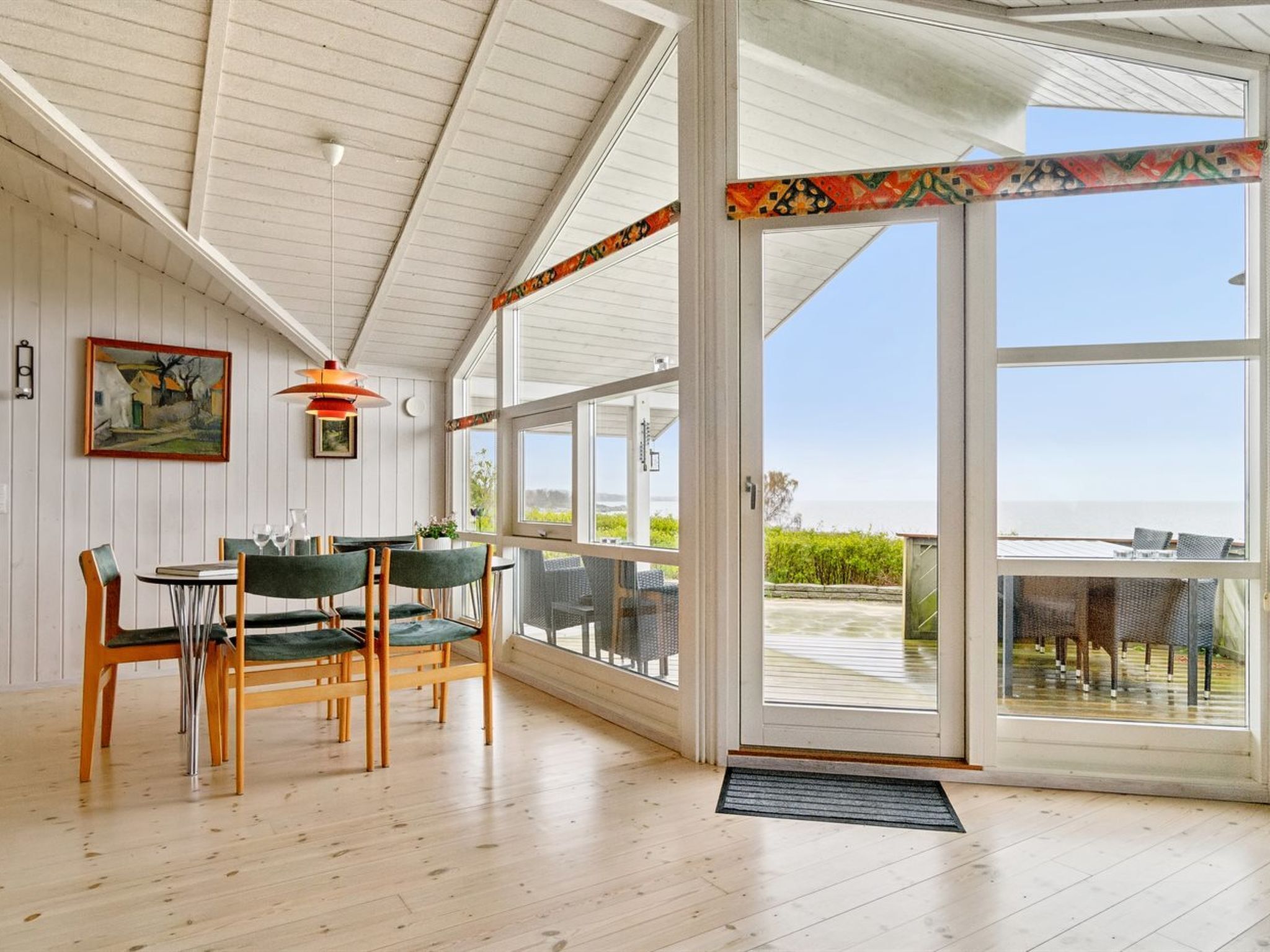 Ein Essbereich mit Tisch und Stühlen, einem Gemälde an der Wand und Blick auf das Meer durch große Fenster.