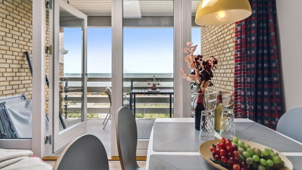 Un balcone con tavolo apparecchiato per mangiare, un vaso con fiori e vista mare.