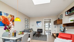 Un soggiorno moderno con zona pranzo, un divano rosso e una cucina visibile attraverso un'apertura.