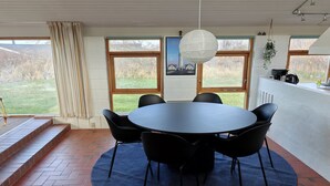 Ein Essbereich mit einem runden Tisch und Stühlen, großen Fenstern und Blick ins Freie.