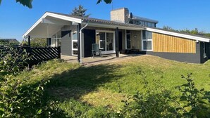 Ein modernes Haus mit überdachter Terrasse, großem Fenster und einer Holzterrasse.