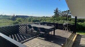 Eine Holzterrasse mit Tisch und Stühlen mit Blick auf eine üppige Landschaft, in der Ferne Windkraftanlagen.