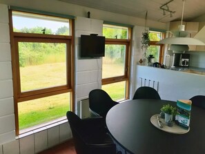 A dining area with a round table, black chairs, and a view of a grassy field through large windows.