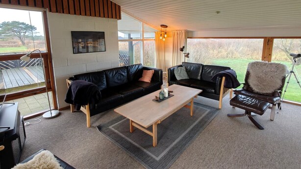 Ein modernes Wohnzimmer mit einem schwarzen Ledersofa, einem Holztisch und einem flauschigen Sessel.