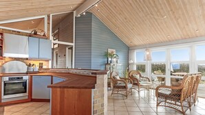 A spacious kitchen with a wooden island, a dining area with wicker chairs, and large windows offering a view of the outdoors.