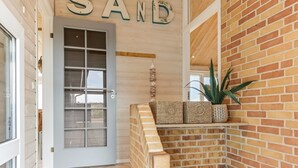 A hallway with a wooden door labeled "SAND," a brick wall, and a small shelf with woven baskets.