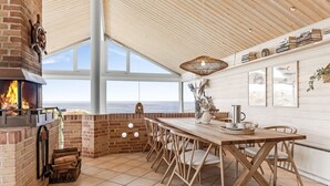 A spacious kitchen with a brick fireplace, a long wooden table, and a view of the ocean.