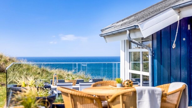 A seaside patio with wicker furniture, a table, and potted plants.