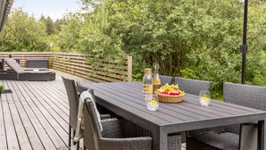 Um deck de madeira com mesa e cadeiras, cercado por vegetação exuberante.