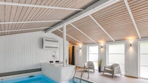 Piscina interior com teto de madeira, um banco embutido e duas cadeiras.