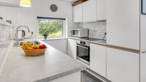 Uma cozinha moderna com armários brancos, micro-ondas embutido, forno e uma cesta de frutas na bancada.