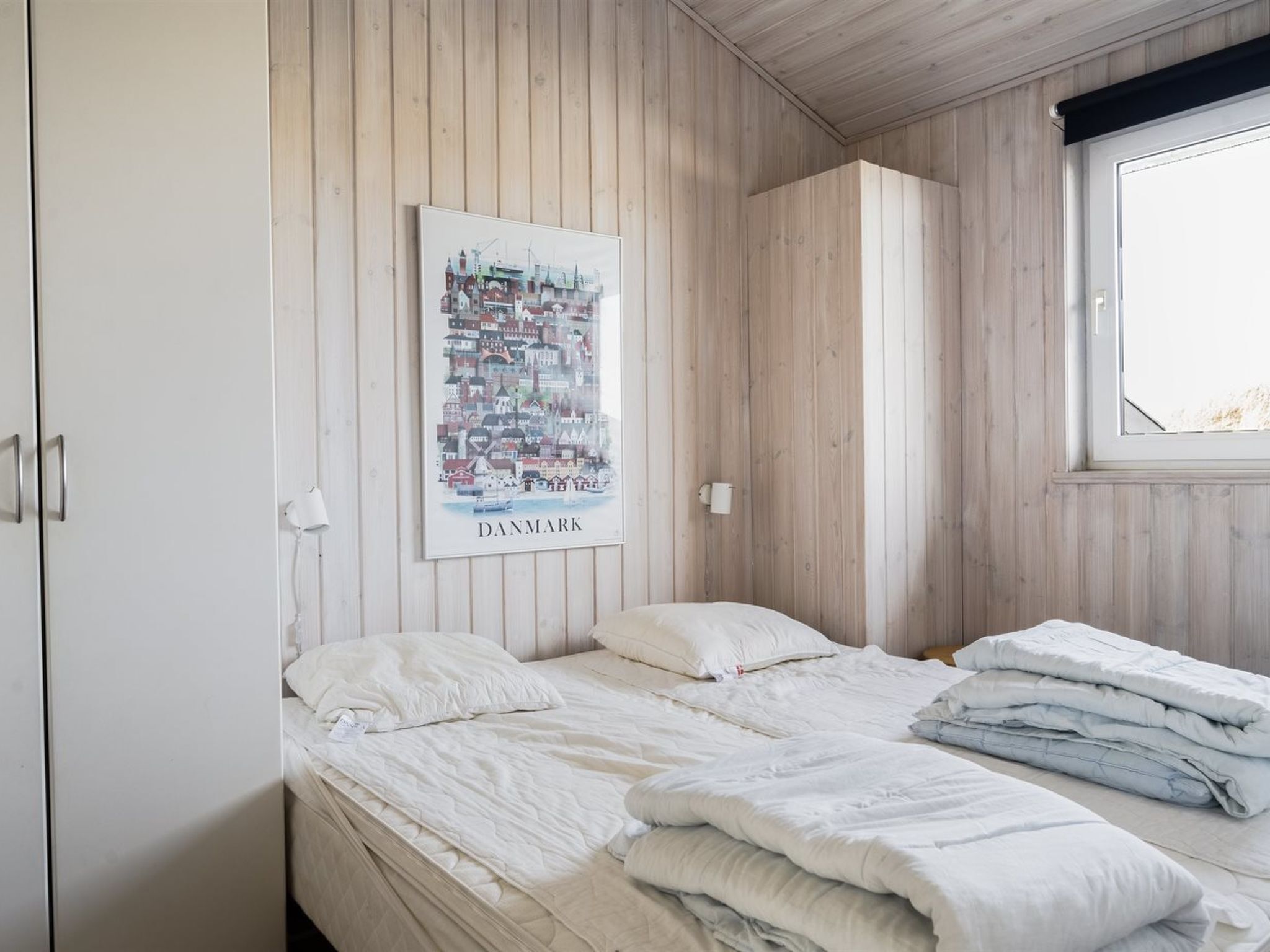 Un dormitorio con pared de paneles de madera, un mapa enmarcado de Dinamarca y una ventana con vistas.
