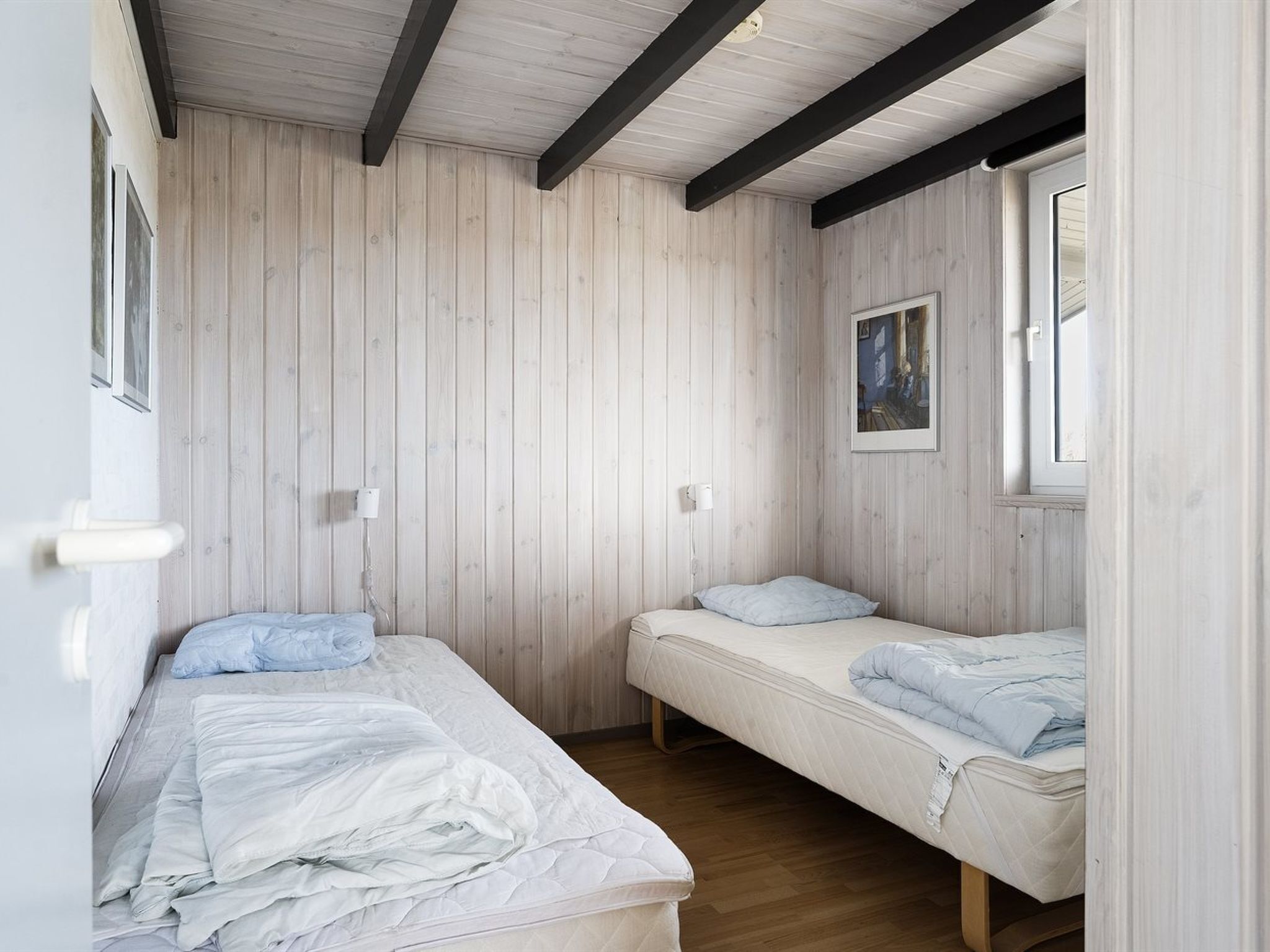 Una habitación con dos camas individuales, paredes de madera, una ventana y un cuadro enmarcado en la pared.