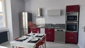 Een moderne keuken met roestvrijstalen apparatuur, een eetgedeelte met een tafel gedekt voor twee personen, en rode keukenkastjes.