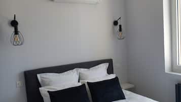 Une chambre à coucher moderne avec un lit, des murs blancs, un ventilateur de plafond et une fenêtre.