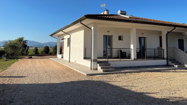A modern house with a covered porch, a gravel driveway, and a view of mountains in the background. - Strategic in the green between Terracina Sabaudia and Circeo (Lazio)