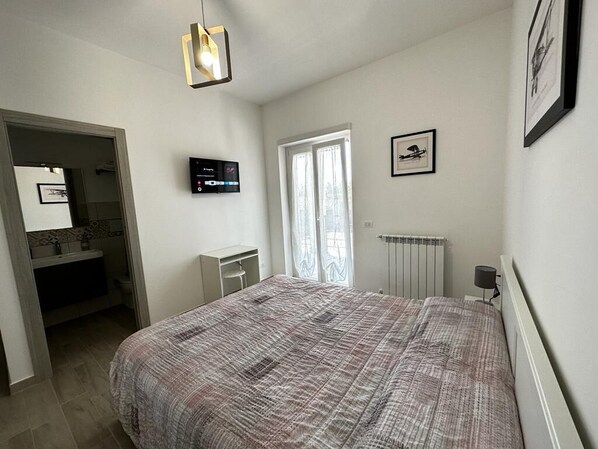 A bedroom with a bed, a TV, a radiator, and a door leading to a bathroom.