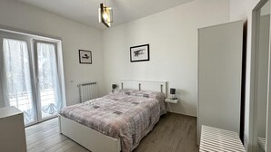 A bedroom with a bed, bedside tables, a radiator, and a window with curtains. - Strategic in the green between Terracina Sabaudia and Circeo (Lazio)