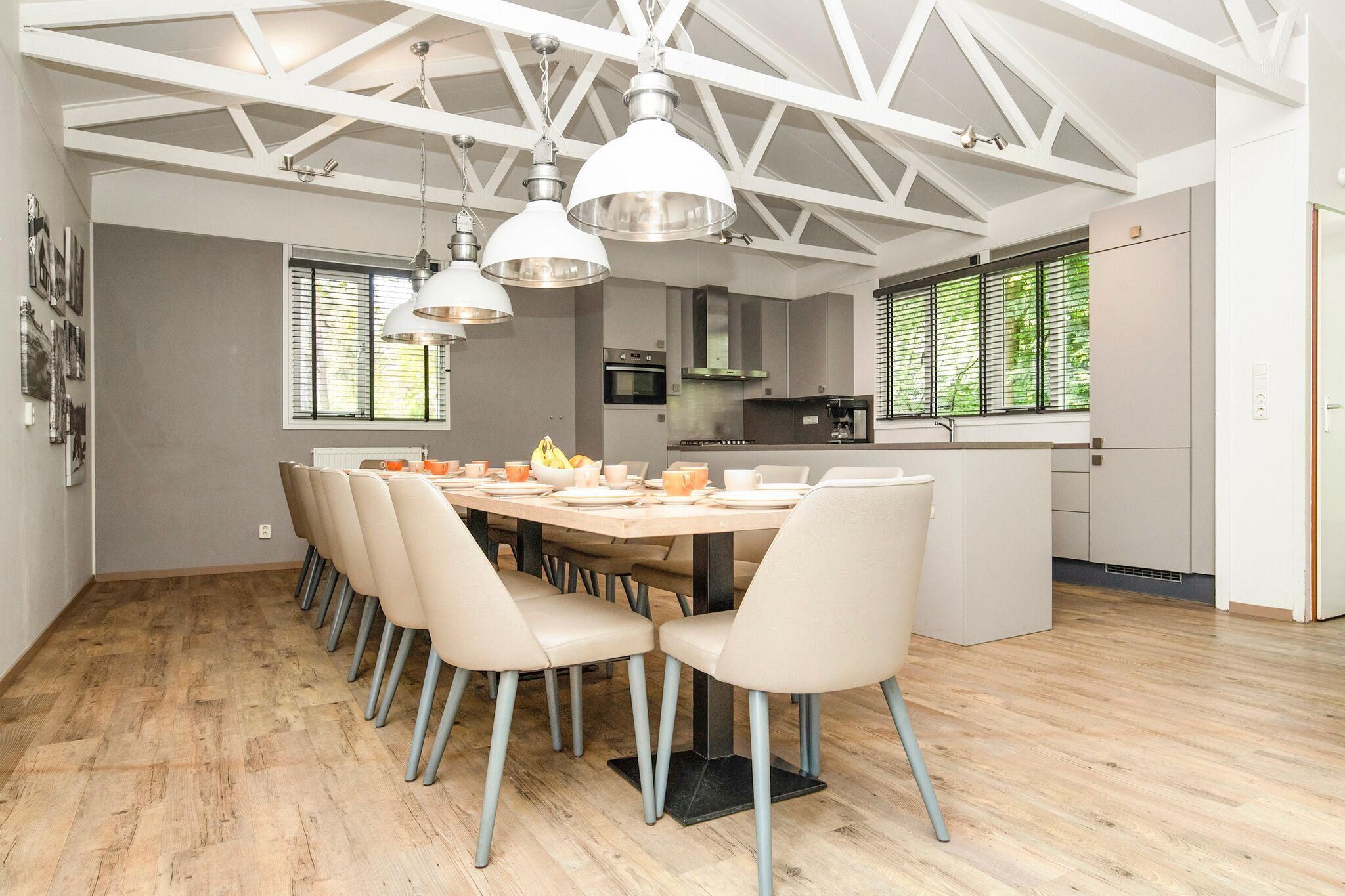 A modern kitchen with a central island, pendant lighting, and a dining area with a long table and chairs.