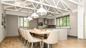 Une cuisine moderne dotée d’un îlot central, de luminaires suspendus et d’un coin repas avec une longue table et des chaises.