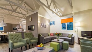 Un salon moderne avec un canapé, des fauteuils, un coin repas et une cuisine en arrière-plan.