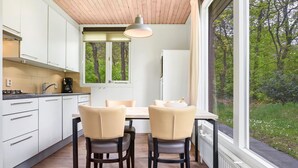 Une cuisine moderne avec des meubles blancs, une table à manger et deux chaises, et une fenêtre donnant sur un jardin.